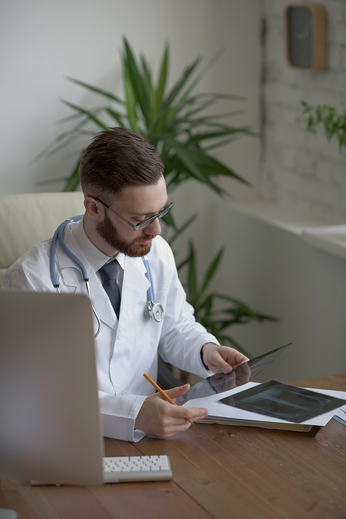 Thoughtful doctor holding chest and lungs xray in medical office