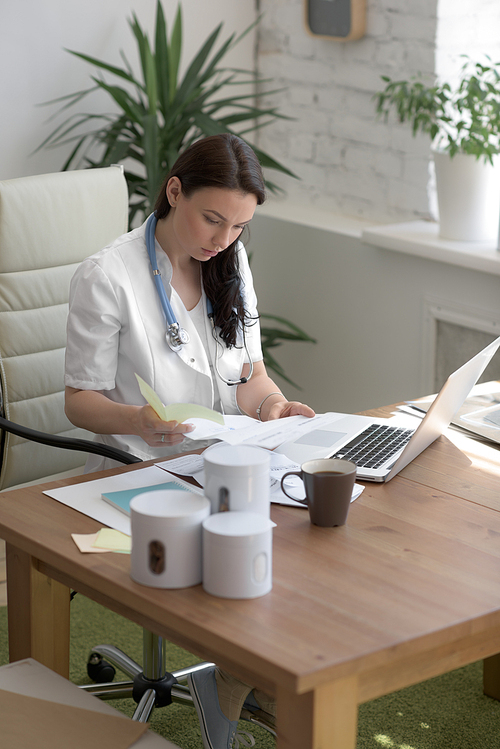 Doctor working with test results and computer at clinic. Filling patient medical record