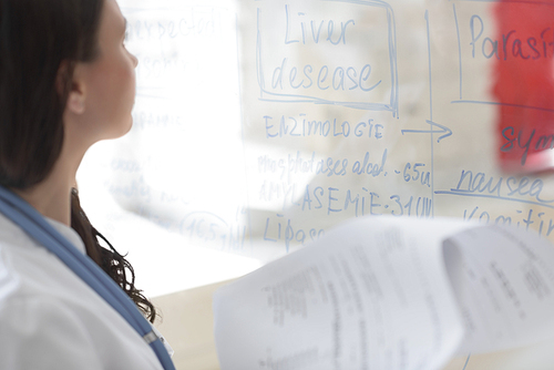 Medical doctor writing patient test results on transparent board to diagnose disease of her patient