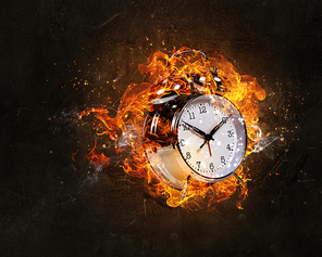 Alarm clock in fire flames on black background