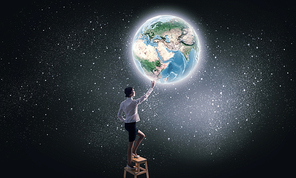 Businesswoman standing on chair and reaching Earth planet. Elements of this image are furnished by NASA