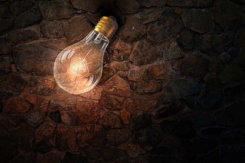 Glass glowing light bulb on stone background