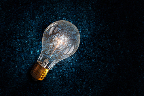 Glowing glass light bulb on soil background