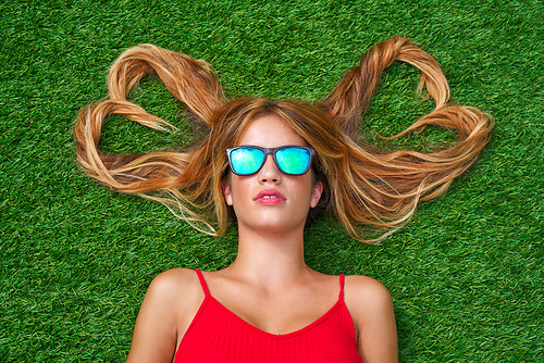 Blond teen girl with hair heart shapes lying down on turf with sunglasses
