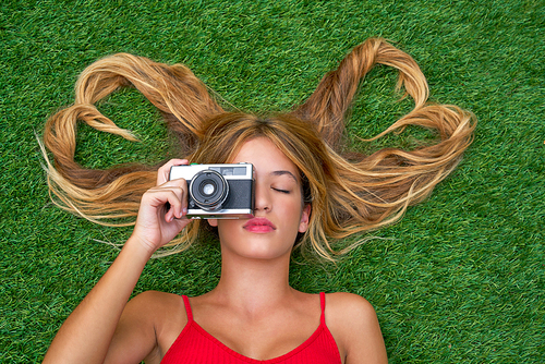 Blond teen girl with hair heart shapes lying down on turf with vintage photo camera
