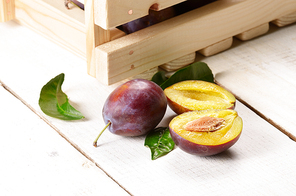 Wooden crate with plums on white table closeup