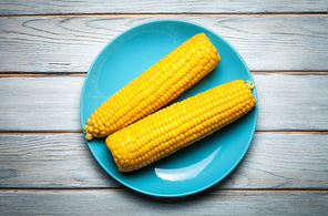 boiled corn on blue plate on white wooden background