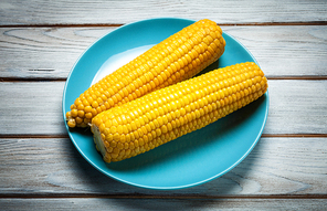 boiled corn on blue plate on white wooden background