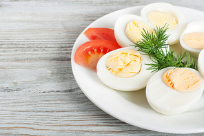 Boiled hen eggs and tomato in a white plate on a wooden background