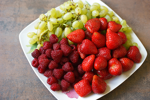 Mix of strawberries, raspberries and grapes on plate, top view