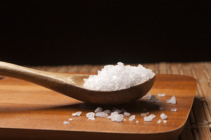 A close up image of a wooden spoon filled with sea salt on a cutting board.