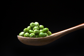 A close up image of green peas on a wooden spoon.