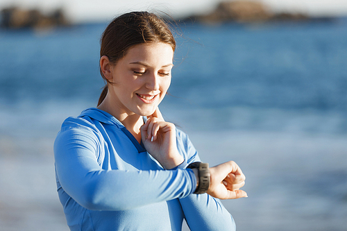 Young runner woman with heart rate monitor running on beach