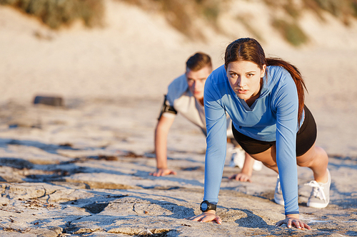 Young couple of man and woman doing push ups on ocean beach