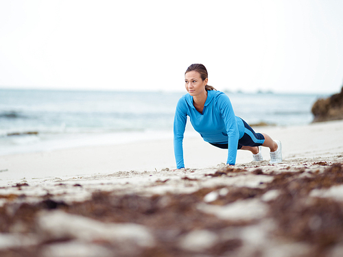 Sporty young woman doing push ups on the sea coast