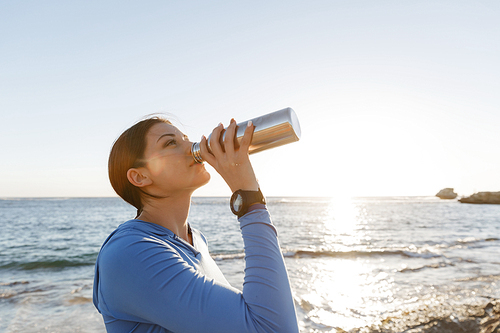 Young woman drinking water after exercising on beach