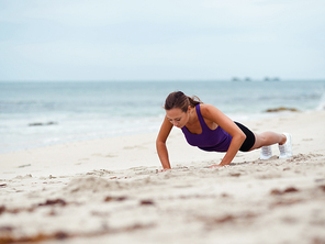 Sporty young woman doing push ups on the sea coast