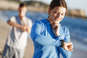 Young runner woman with heart rate monitor running on beach