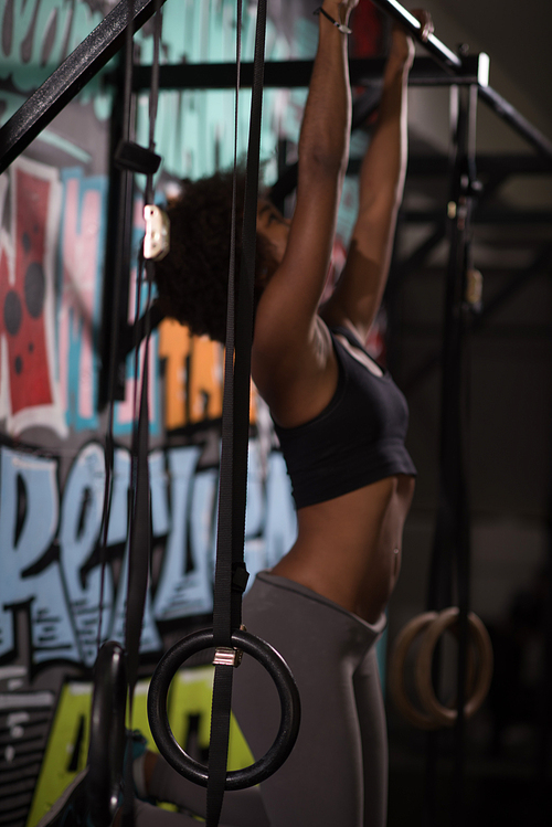 young beautiful african american woman athlete doing pull ups on the horizontal bar in the gym