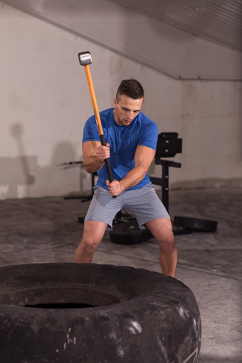 Sledgehammer Tire Hits young muscular man workout at gym with hammer and tractor tire