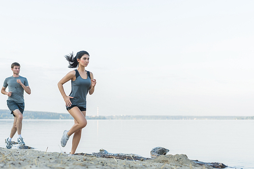 Cheerful Hispanic Caucasian couple running on beach at morning