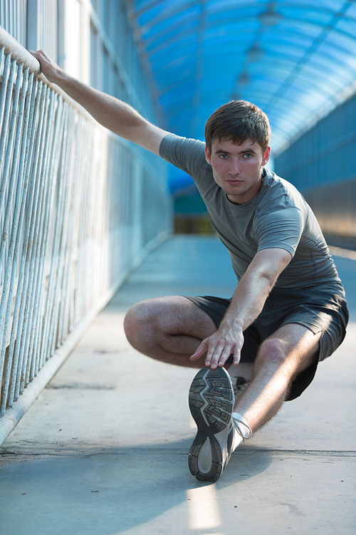 Attractive fit young man stretching before exercise, sunrise early morning backlit. Shallow depth of field