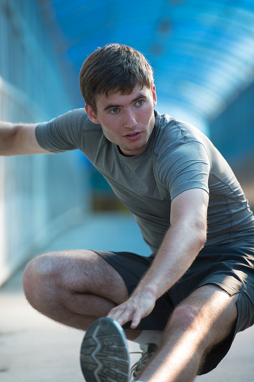 Attractive fit young man stretching before exercise, sunrise early morning backlit. Shallow depth of field