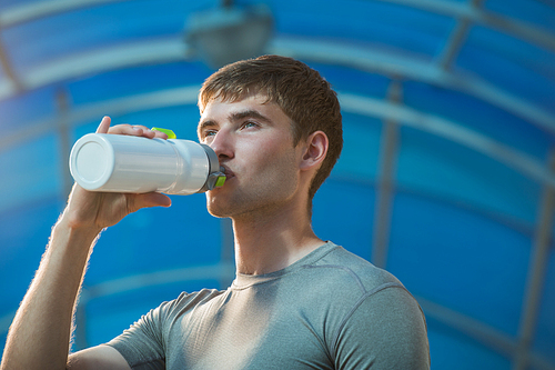 Athletic young man drinking water after hard training