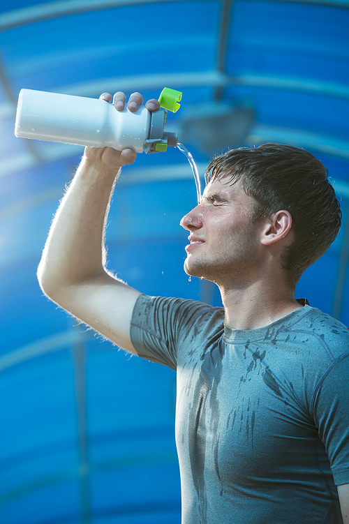 Young tired athlete splashing and pouring fresh water on his head to refresh during a running trail