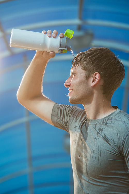 Athletic young man drinking water after hard training