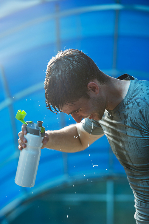 Young tired athlete splashing and pouring fresh water on his head to refresh during a running trail