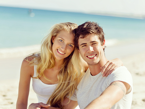 Romantic young couple sitting on the beach looking at the ocean