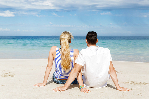 Romantic young couple sitting on the beach looking at the ocean