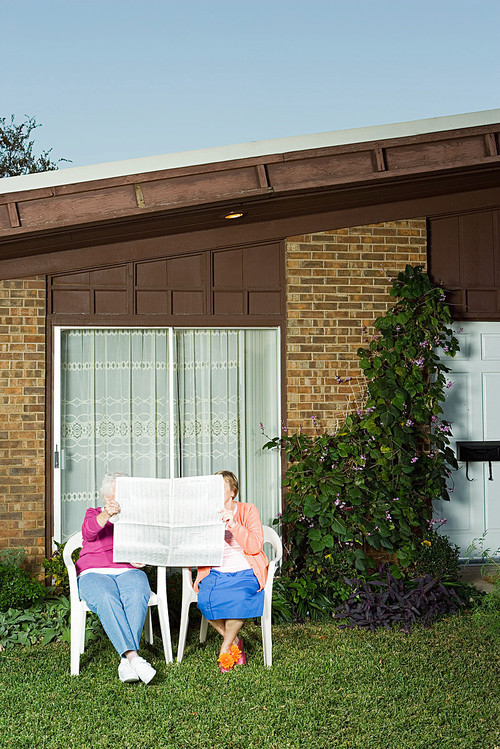 Two senior women sharing a newspaper