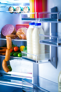 Open refrigerator filled with food. Focus on Bottles of milk in the fridge