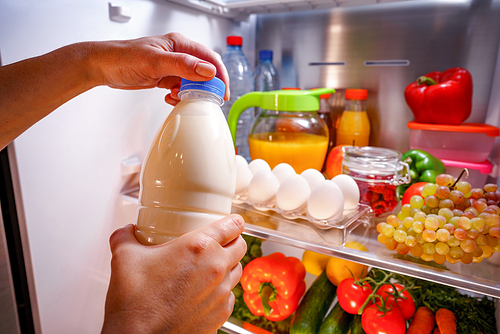 Woman takes the milk from the open refrigerator
