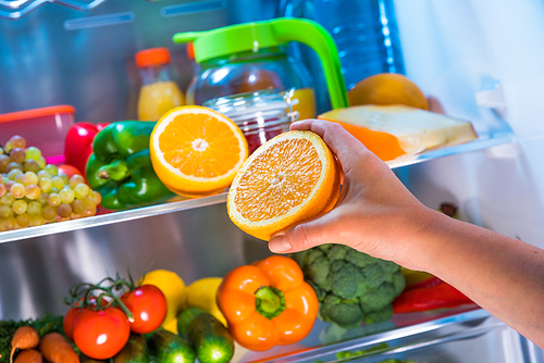 Woman takes the orange from the open refrigerator. Healthy food.