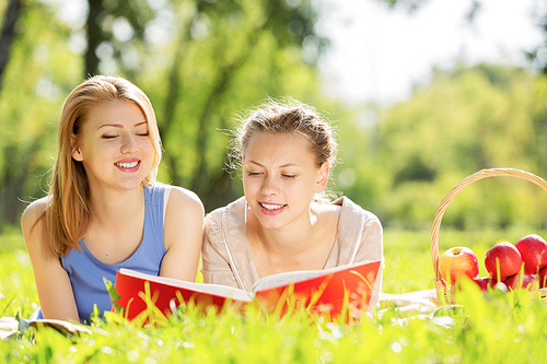 Young pretty girls in summer park reading book