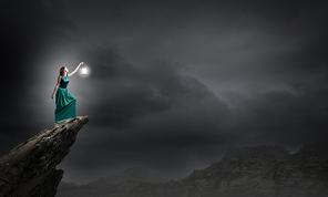 Young woman in green dress with lantern walking in darkness