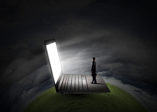 Young businessman with briefcase standing on huge laptop