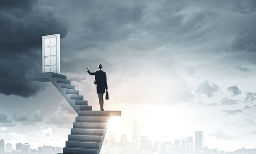 Businesswoman walking up staircase to door in sky