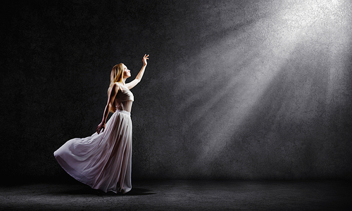 Young woman in white long dress reaching to light