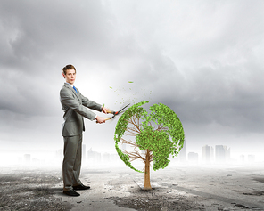 Young businessman cutting tree with scissors in shape of Earth planet