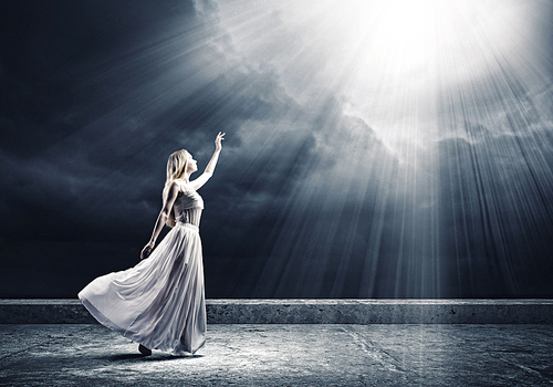 Young woman in white long dress reaching to light