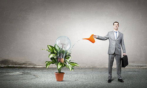 Young cheerful businessman watering green sprout with can