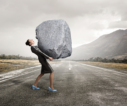 Attractive businesswoman carrying big heavy stone