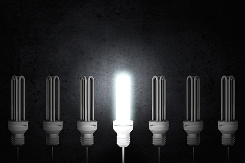 Light bulbs on dark background with one glowing
