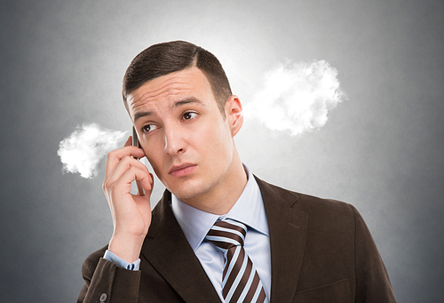 Portrait of a man with steam from his ears calling by mobile phone