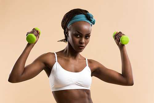 Beautiful african woman pumping up muscles with dumbbells