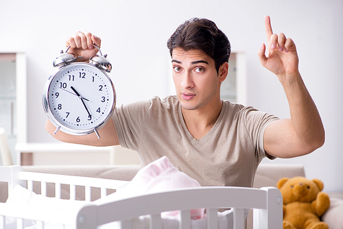 Young dad with clock near newborn baby bed cot